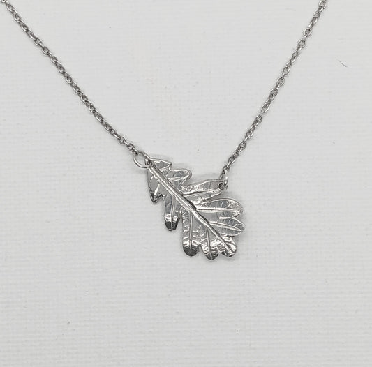 detail of hand carved sterling silver oak leaf attached from the end and midpoint to a chain so that it hangs at an angle