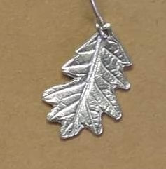 detail of hand carved sterling silver oak leaf dangling from its stem on an earring hook