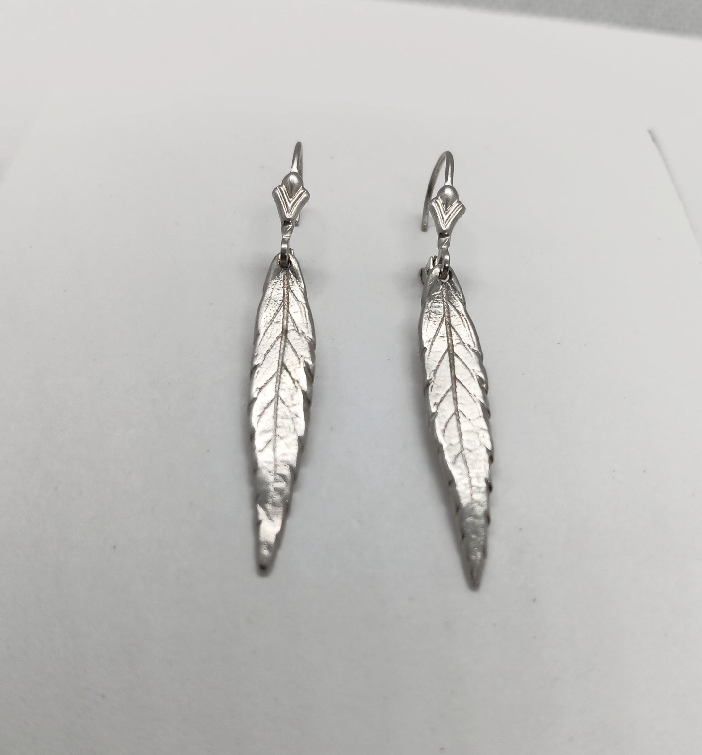 vein detail of a single lobe of a cannabis leaf is visible in sterling silver dangle as discrete earrings