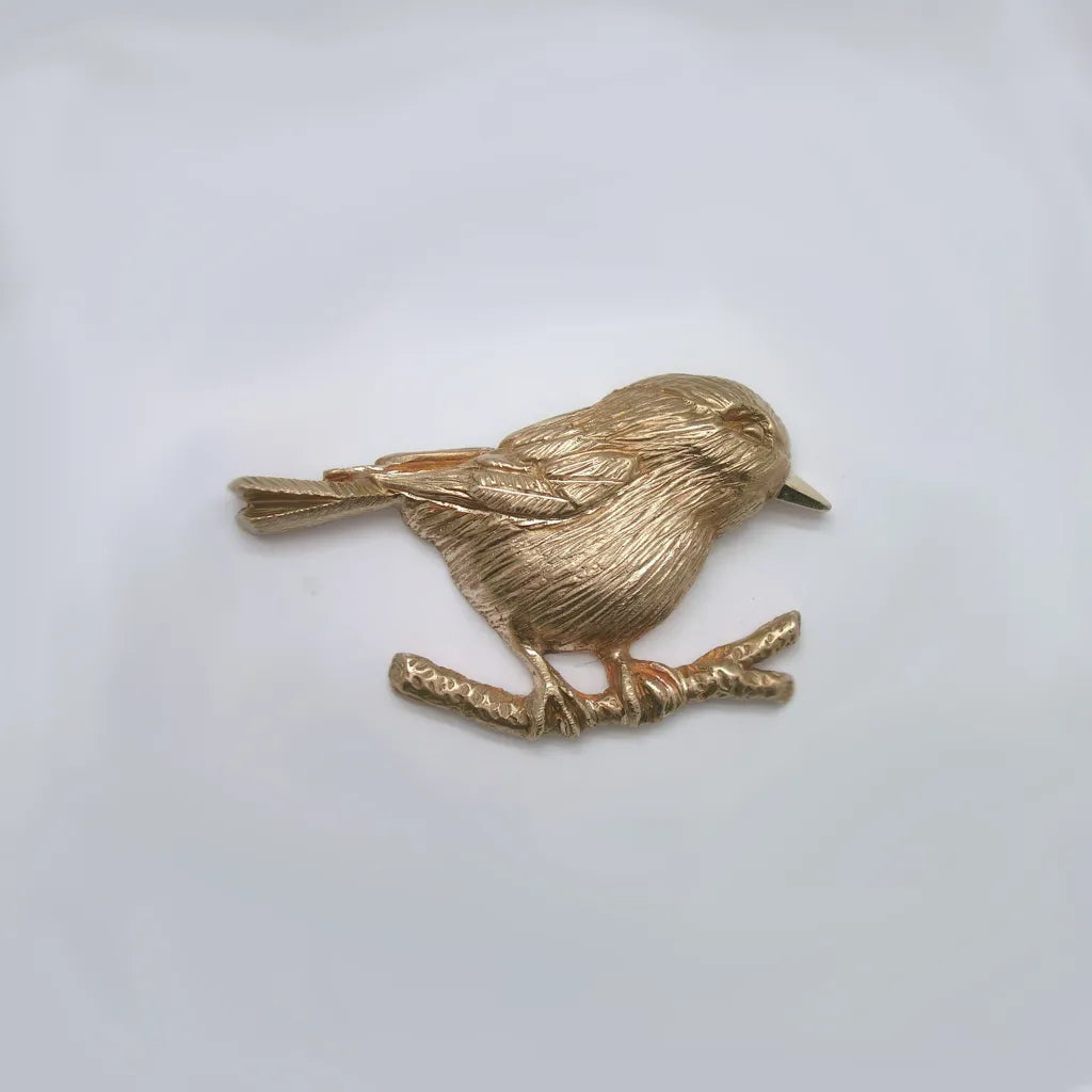 Close up showing fine feather detail of one-sided hand carved shiny bronze chickadee perched on a branch on a white background