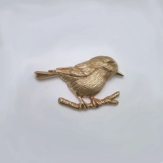 Close up showing fine feather detail of one-sided hand carved shiny bronze chickadee perched on a branch on a white background