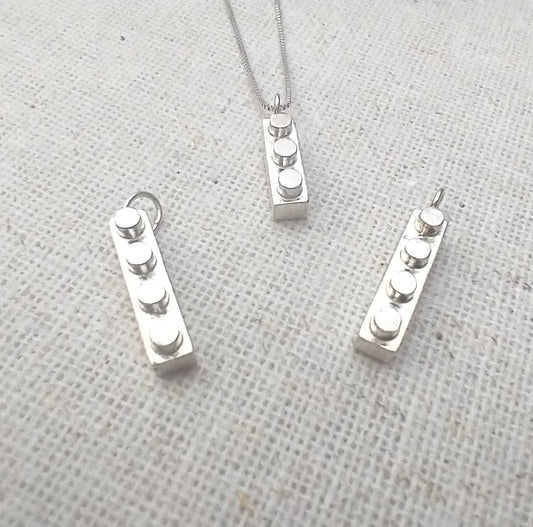 several shiny sterling silver Lego block keepsakes with 3 or 4 studs each and a loop on one end for hanging on a necklace