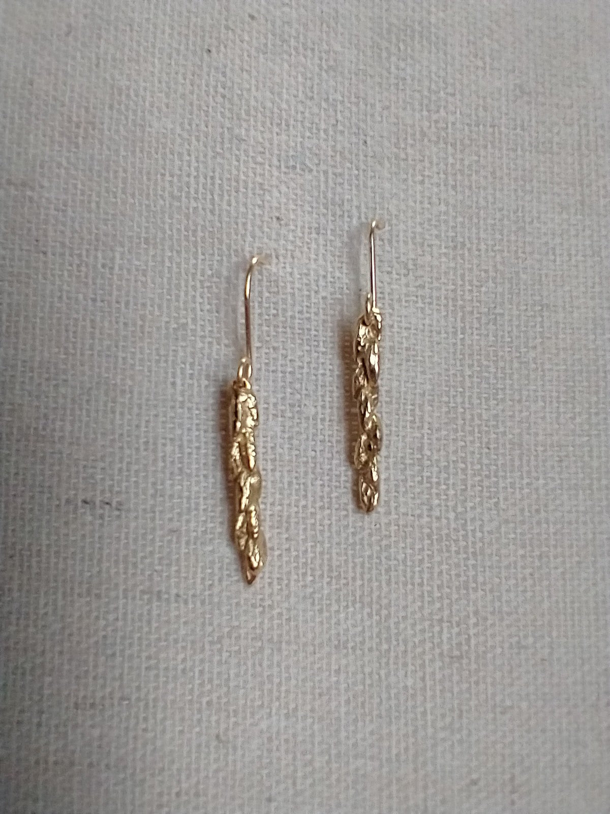 detail of 5 rows of wheat kernels are visible on a small stalk of the shiny bronze cast earrings on gold wire hooks