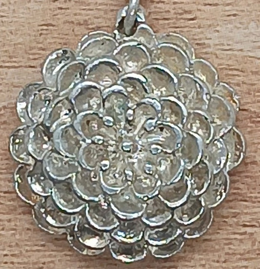 close up view of the Five concentric circles of delicate round petals layering up on brilliantly shiny hand carved sterling silver dahlia pendant