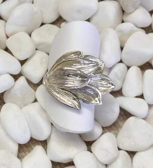 7 delicately detailed shiny silver petals lie stacked from one point on the ring, laying gently curved horizontally over the wide silver band