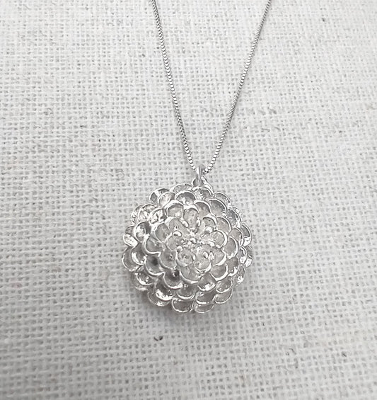 Five concentric circles of delicate round petals layer up toward the centre of this shiny hand carved sterling silver dahlia pendant