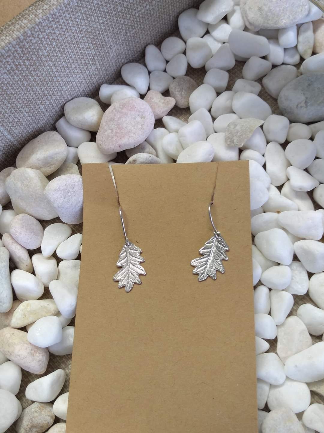 pair of approximately 1 inch long hand carved sterling silver oak leaf earrings dangling from their stems on earring hooks
