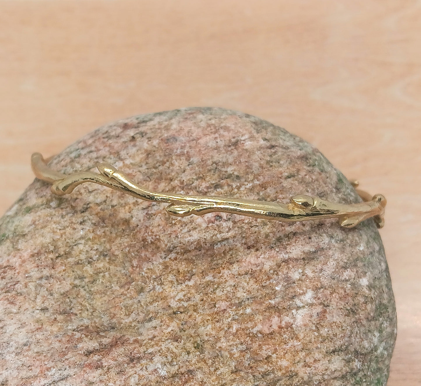 close up of a delicate shiny bronze twig with tiny buds alternating along the length, formed as a closed circle bracelet