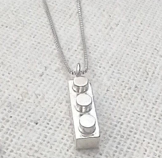shiny sterling silver 3-stud Lego block keepsake with a loop on one end for hanging from delicate chain shown