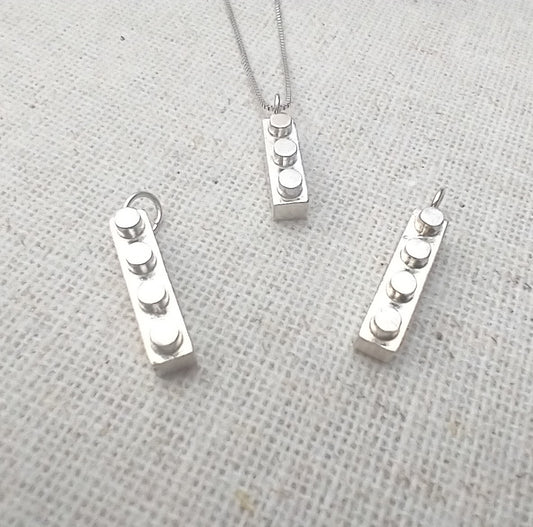several shiny sterling silver Lego block keepsakes with 3 or 4 studs each and a loop on one end for hanging on a necklace