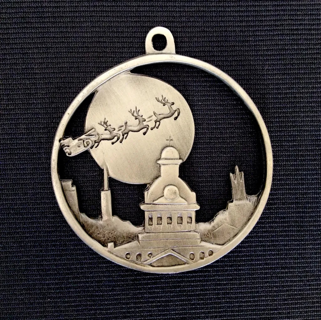 Finely detailed scene of a team of reindeer pulling Santa’s sleigh skyward in front of the Moon, over Kingston’s iconic skyline on a dark background (palm sized, single-sided round, die-cast pewter)