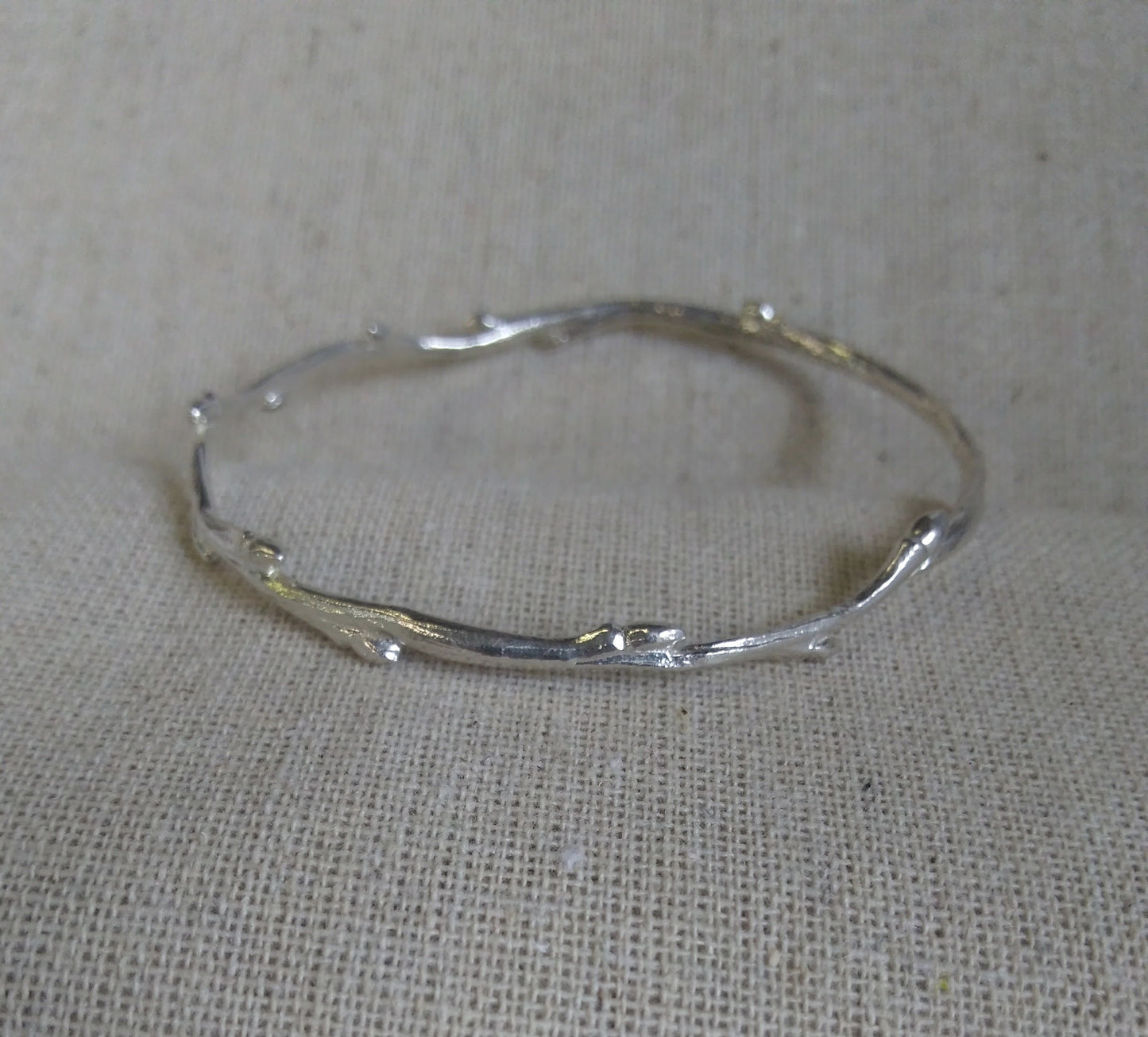 close up of a delicate shiny silver twig with tiny buds alternating along the length, formed as a closed circle bracelet