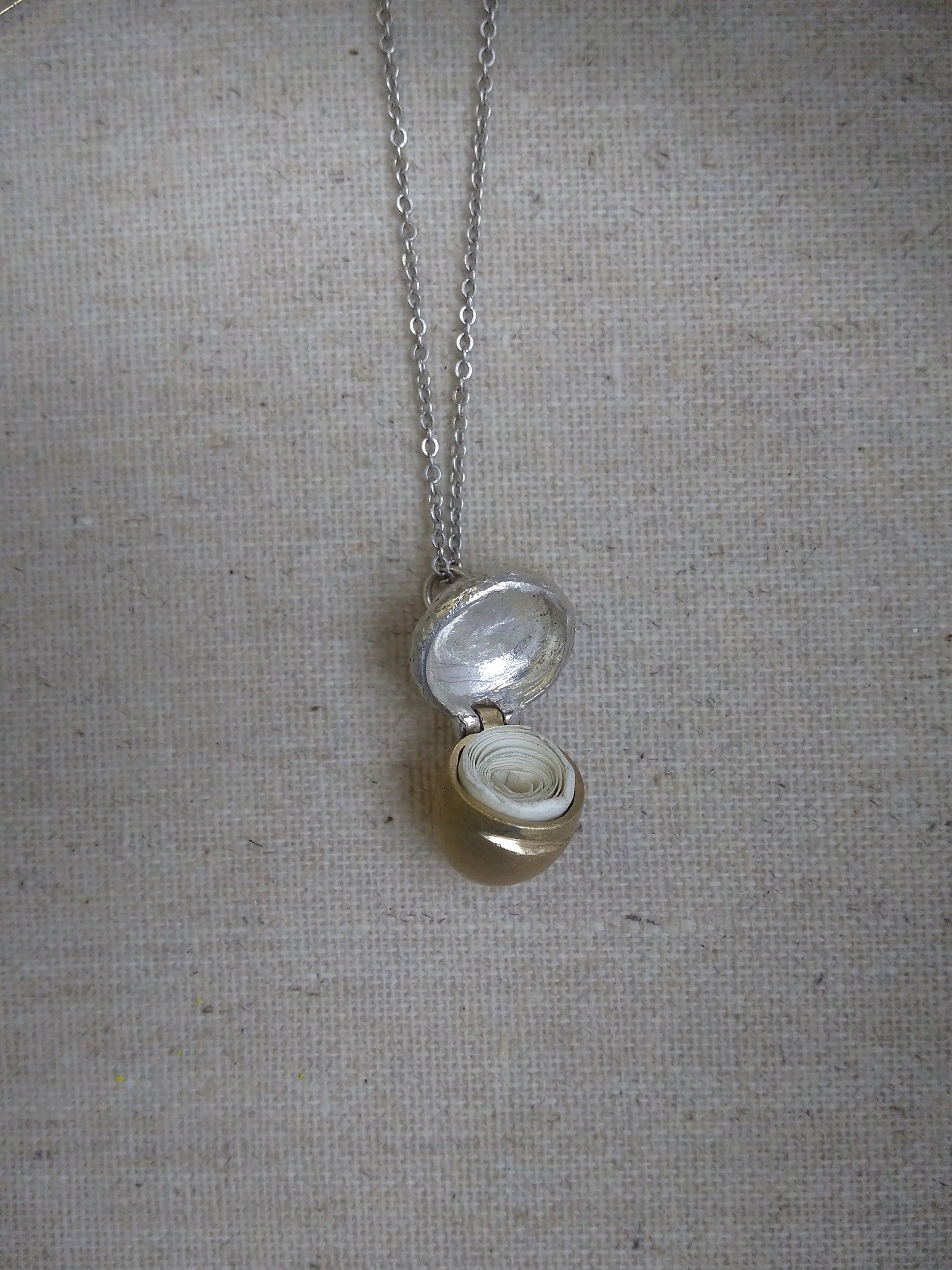 Detail of shiny silver acorn locket with cap hinged open showing the coiled paper note inside