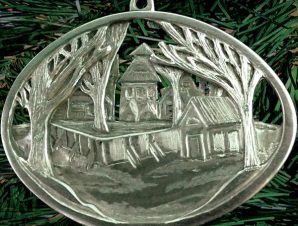 Finely detailed oval scene of bare trees and skating rink boards in a city park with backdrop of neighbourhood houses (palm sized, single-sided die-cast pewter)